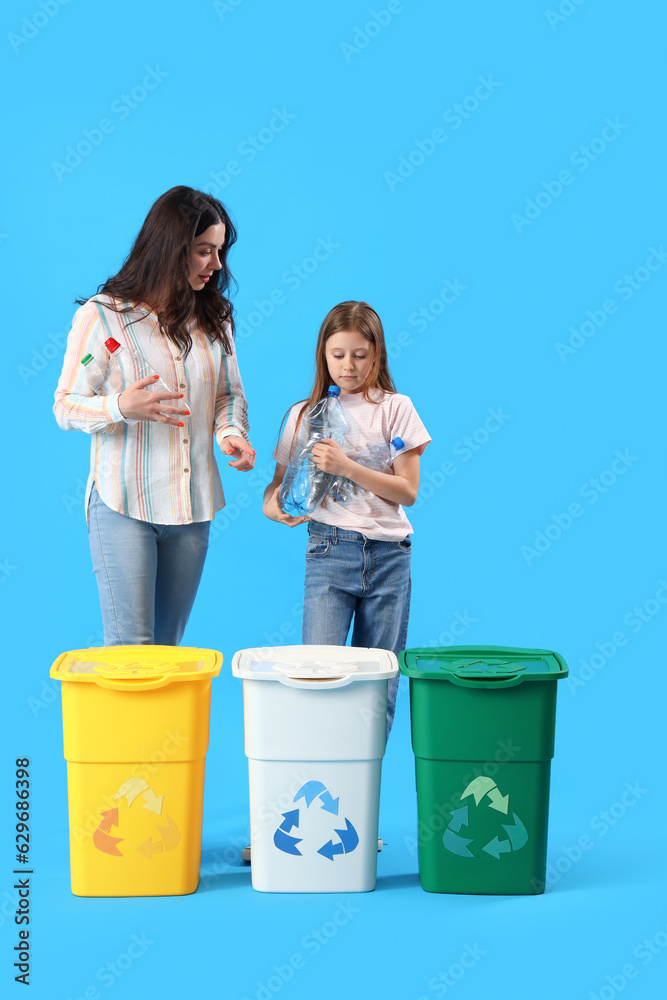 Little girl with her mother throwing plastic bottles in recycle bin on blue background