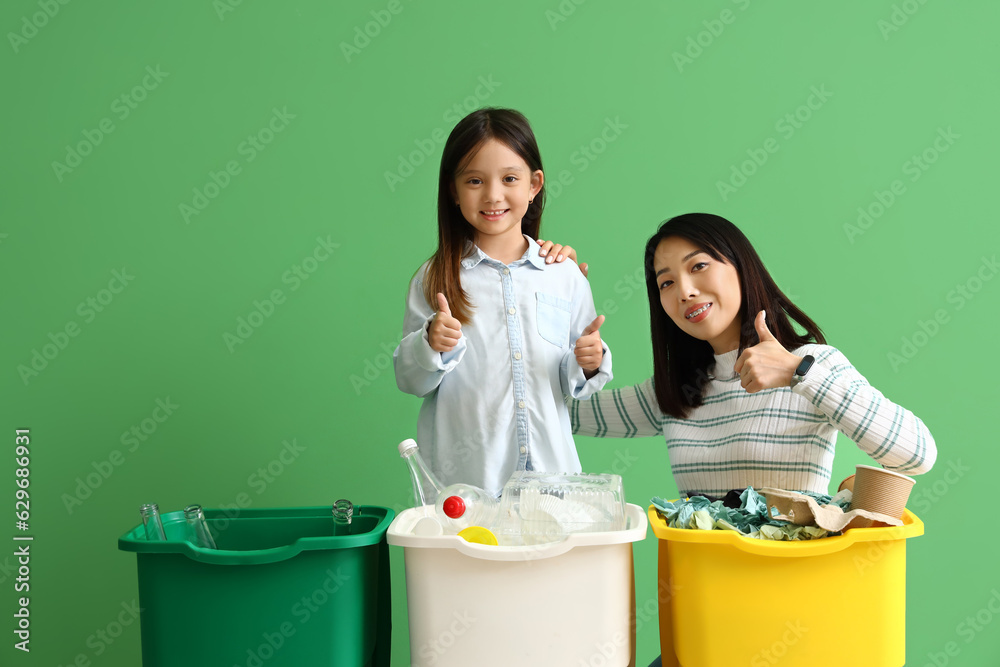 Asian mother with her little daughter sorting garbage in recycle bins on green background