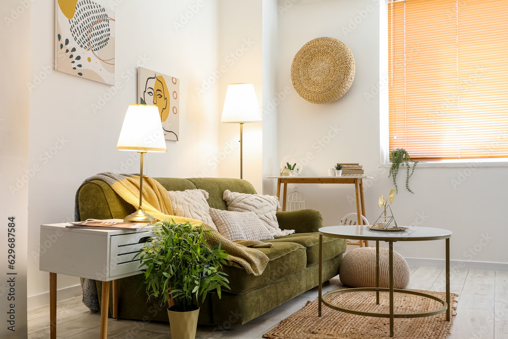 Interior of stylish living room with cozy green sofa, coffee table and glowing lamps