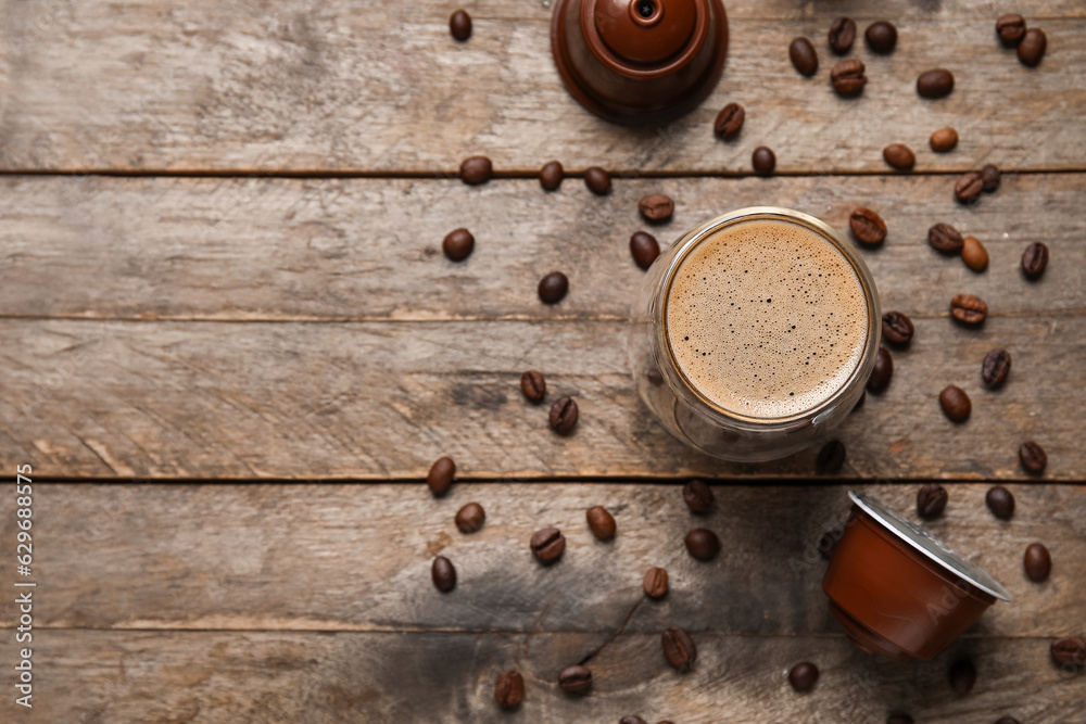 Glass of delicious coffee, pods and beans on wooden table