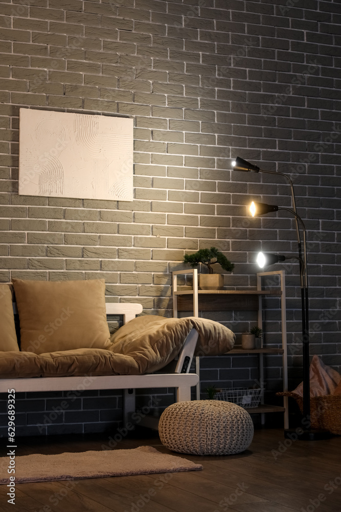 Interior of dark living room with glowing lamps, couch and shelving unit