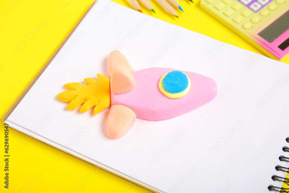 Rocket made of plasticine and stationery on yellow background