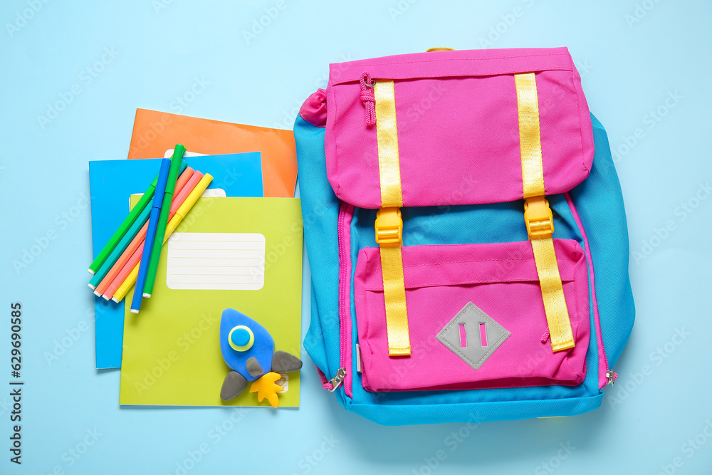 Backpack with rocket made of plasticine and stationery on blue background