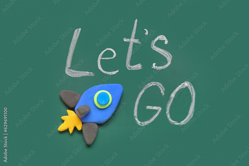 Rocket made of plasticine with text LETS GO on green chalkboard