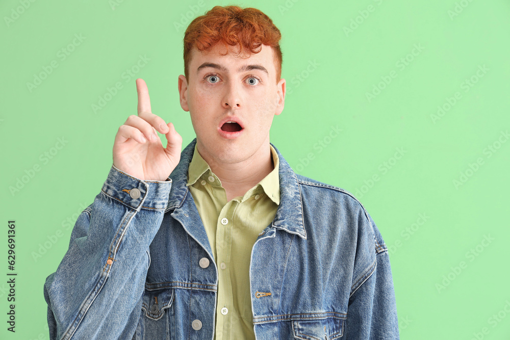 Young redhead man pointing at something on green background