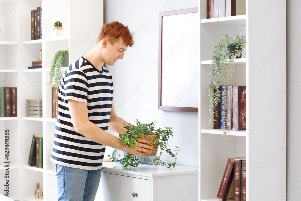 Young redhead man with houseplant at home