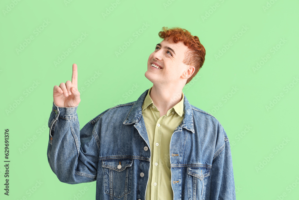 Young redhead man pointing at something on green background