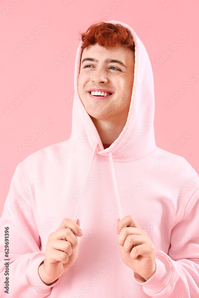 Young redhead man in hoodie on pink background, closeup