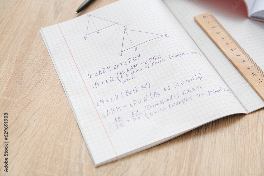 Open copybooks with math formulas and ruler on wooden table, closeup