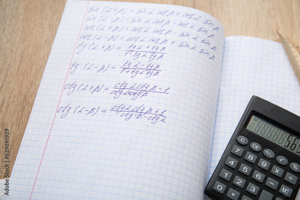 Open copybooks with math formulas and calculator on wooden table, closeup