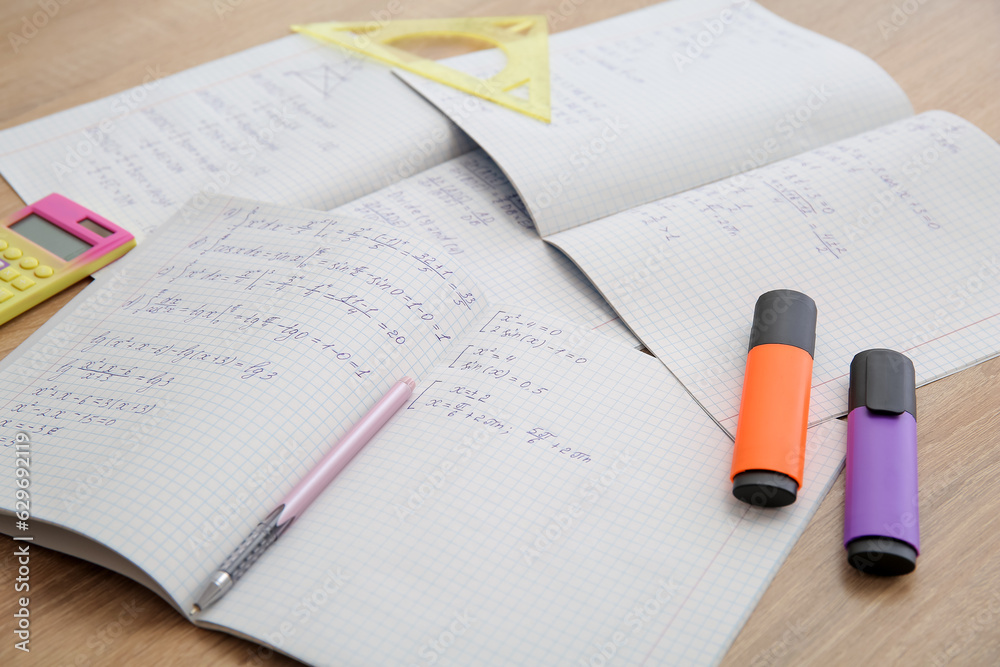 Open copybooks with math formulas and stationery on wooden table