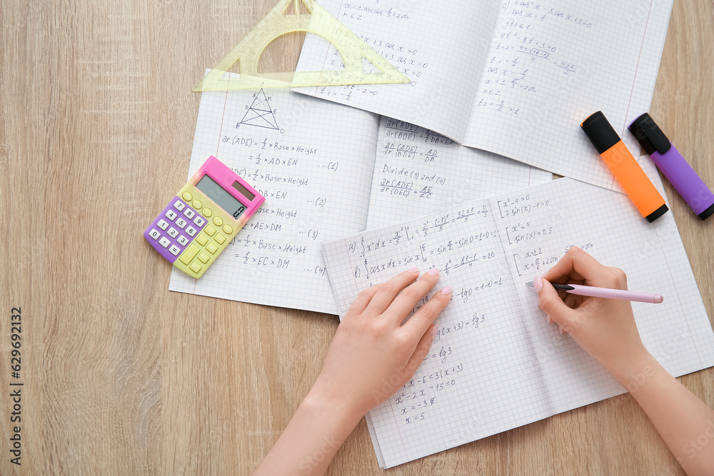 Woman writing math formulas in copybook on wooden table