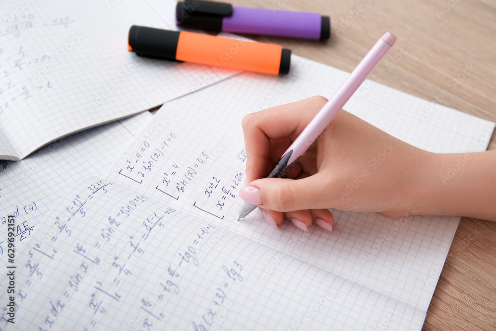 Woman writing math formulas in copybook on wooden table