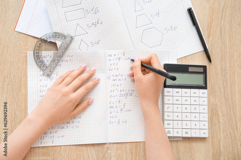 Woman writing math formulas in copybook on wooden table