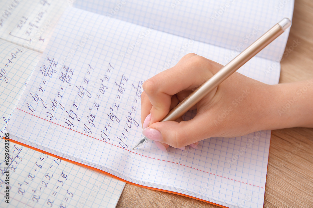 Woman writing math formulas in copybook on wooden table