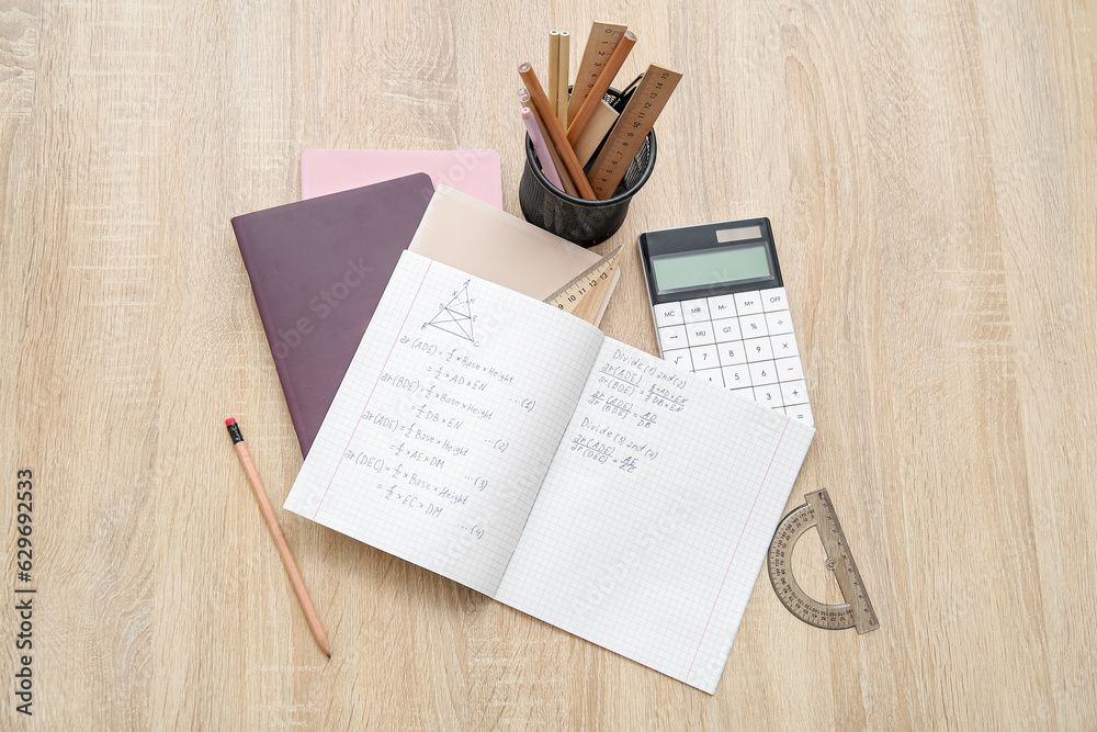 Open copybooks with math formulas and stationery on wooden table