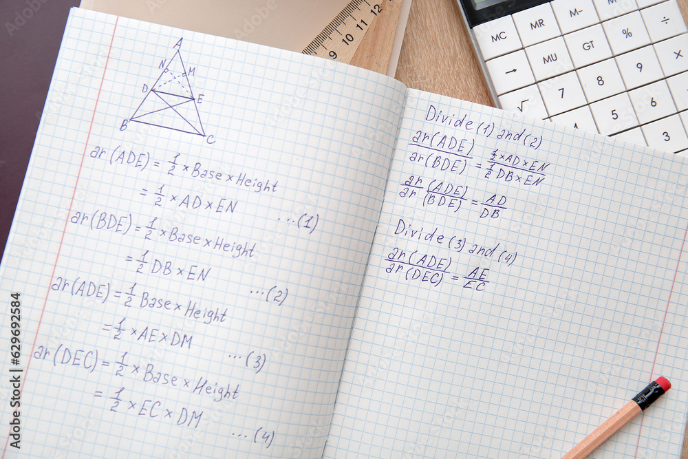 Open copybook with math formulas on wooden table, closeup