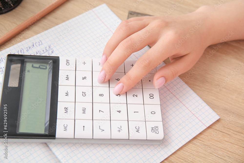 Woman working with calculator on wooden table, closeup