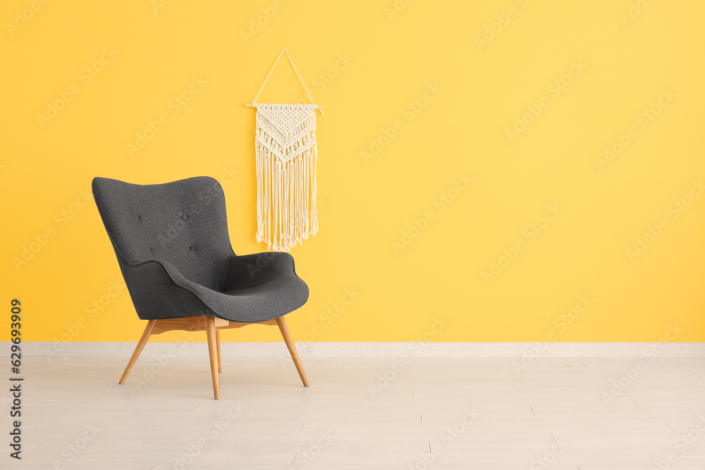 Stylish black armchair and wicker decor near yellow wall