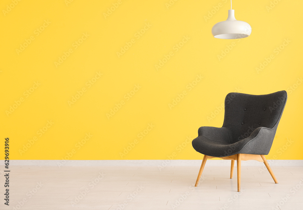 Stylish black armchair and lamp near yellow wall