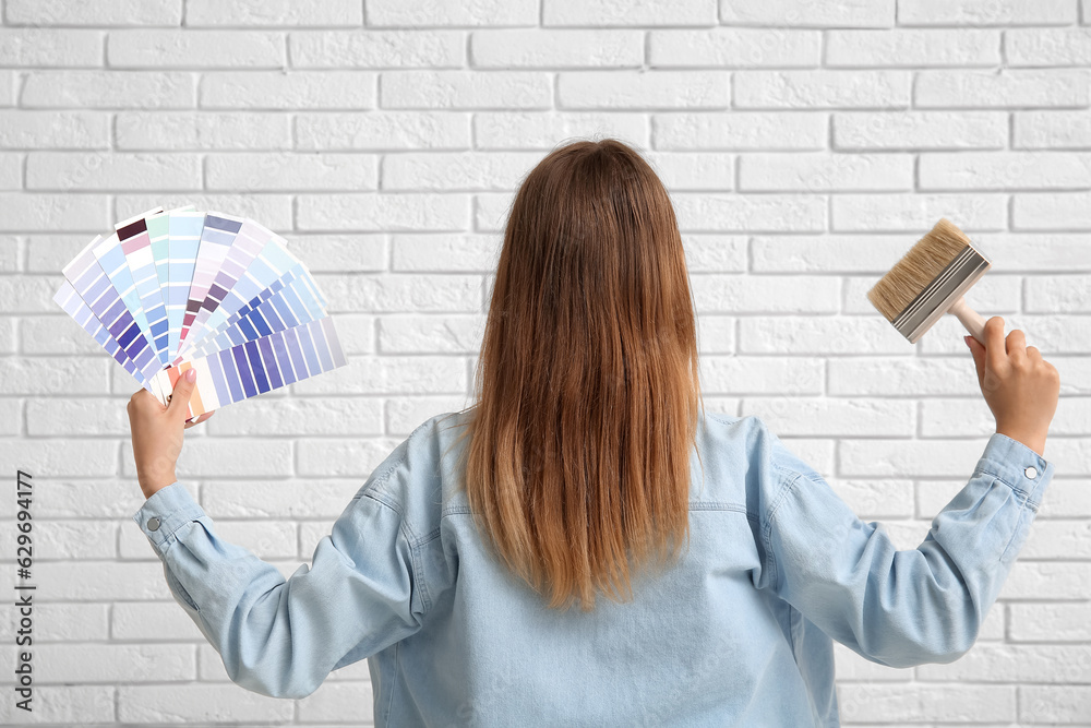 Young woman with color samples and brush on white brick background, back view