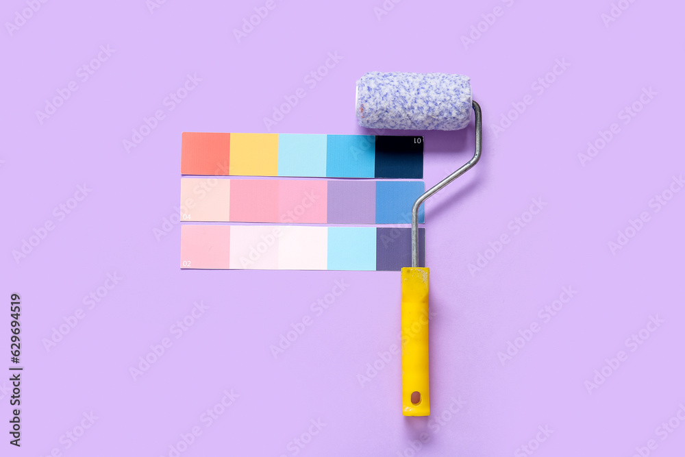 Many color palettes and paint roller on lilac background, top view