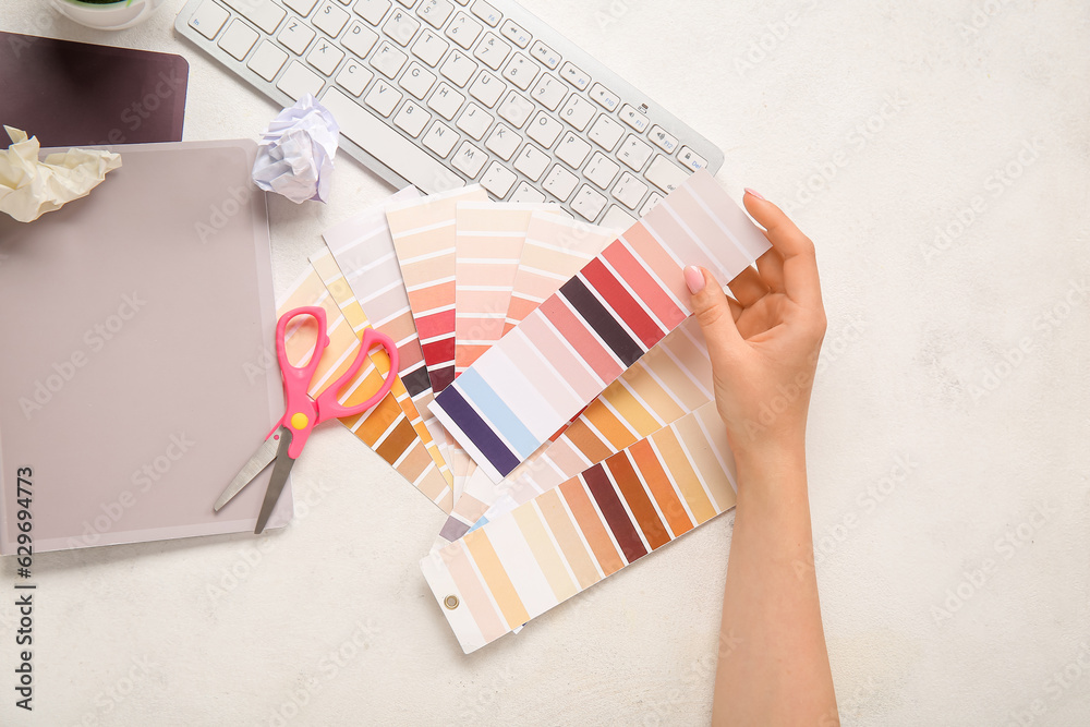 Female hand, color palettes, PC keyboard, notebooks and scissors on light background