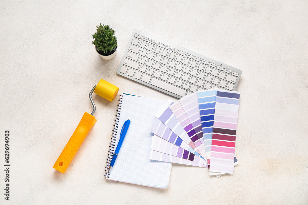 Many color palettes, PC keyboard, paint roller and notebook on light background, top view