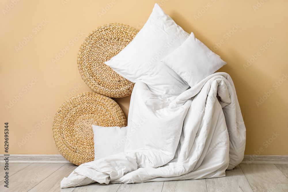 White pillows, blanket and wicker poufs near beige wall