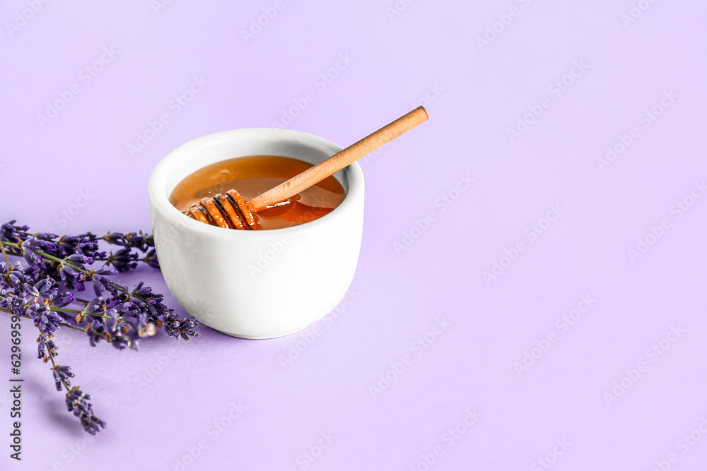 Bowl of sweet lavender honey, dipper and flowers on lilac background