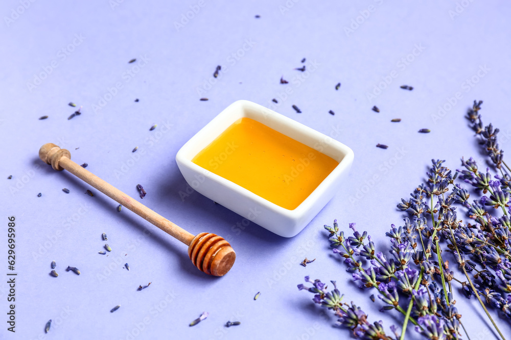 Bowl of sweet lavender honey, dipper and flowers on blue background