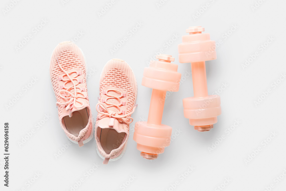 Pair of sneakers and dumbbells on white background