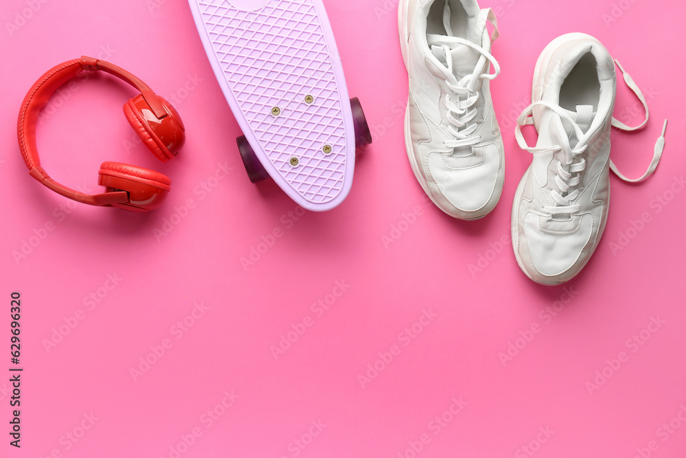 Pair of sneakers, skateboard and headphones on pink background