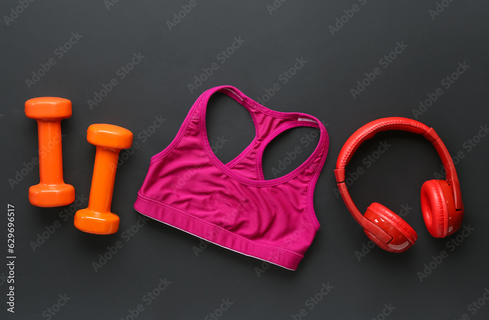 Dumbbells, sports bra and headphones on dark background