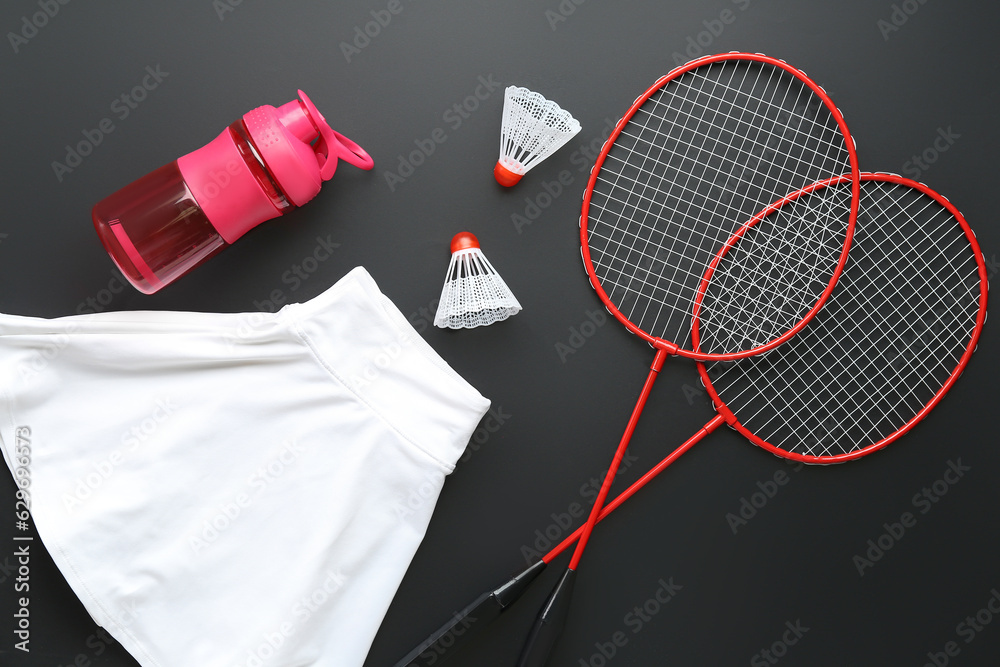 Badminton rackets, shuttlecocks, bottle of water and sportswear on dark background