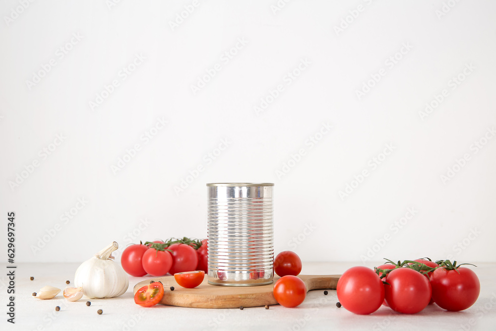 Tin can with tomatoes and spices on light background