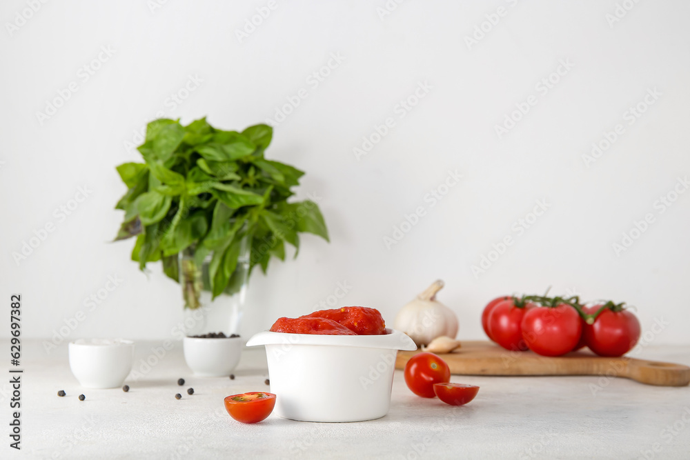 Bowl of canned tomatoes and spices on light background