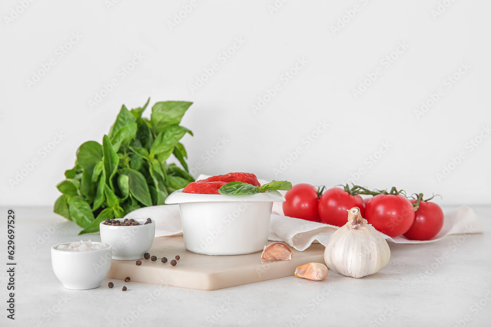 Bowl of canned tomatoes and spices on light background