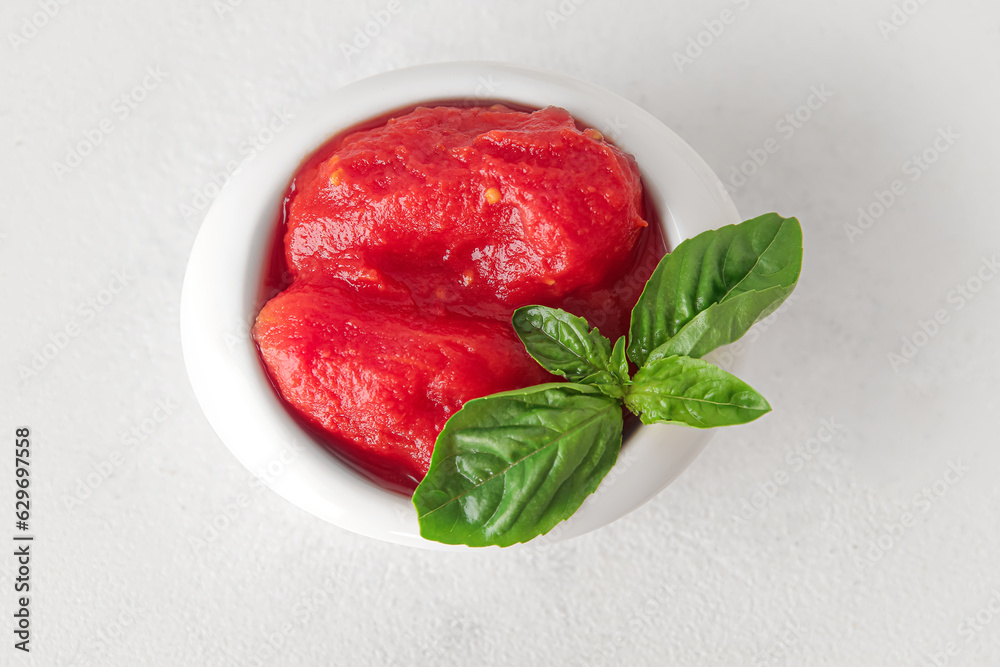 Bowl of canned tomatoes with basil on light background