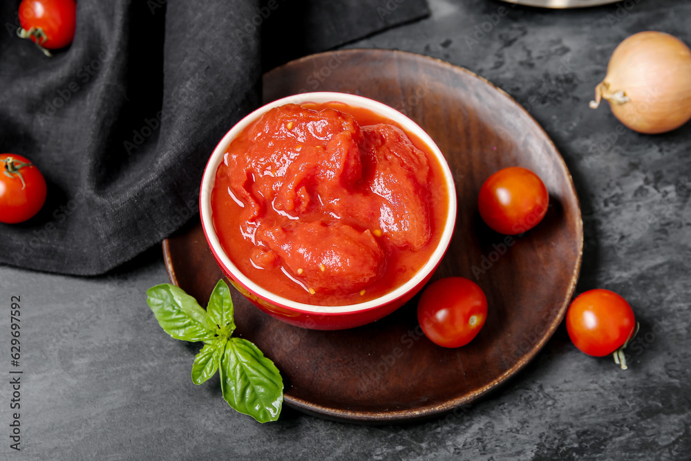 Bowl of canned and fresh tomatoes on dark background