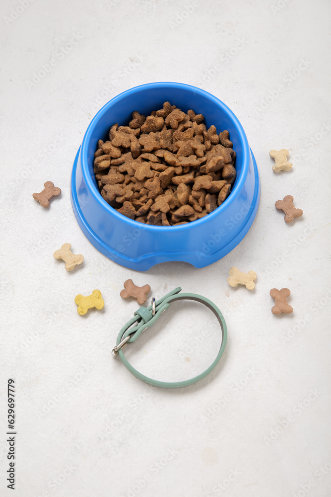 Pet collar and bowl of dry food on light background