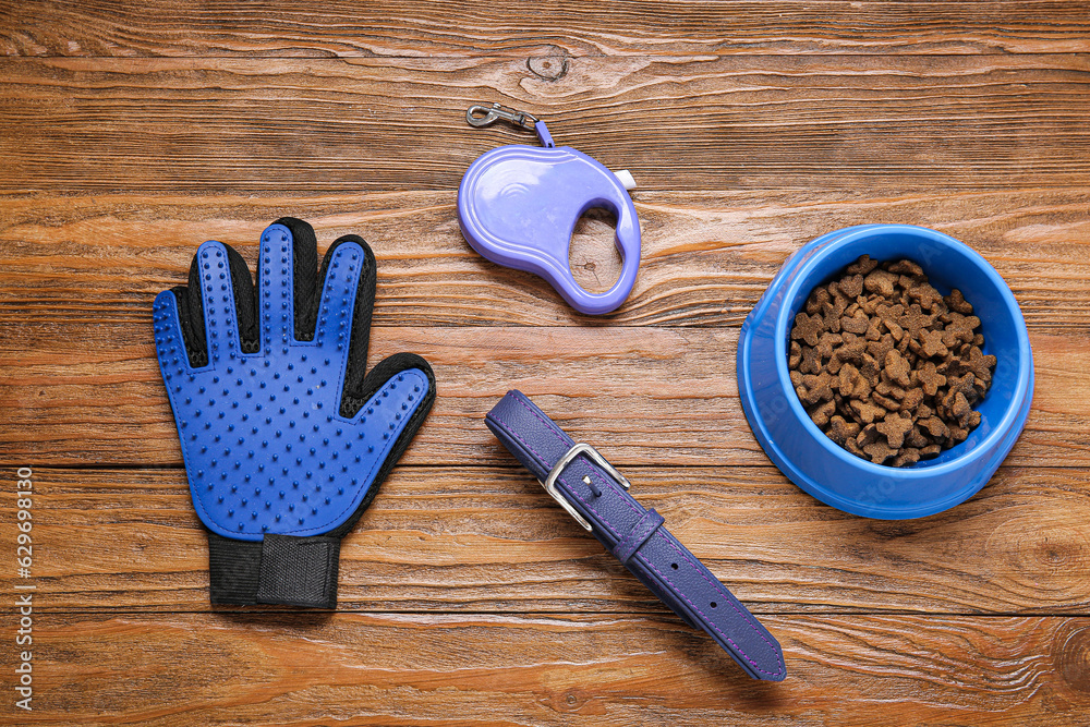 Bowl of dry pet food, leash, collar and grooming glove on wooden background