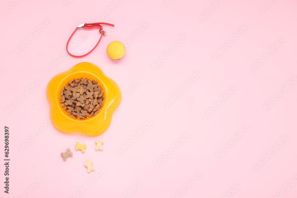 Bowl of dry pet food, collar and toy ball on pink background