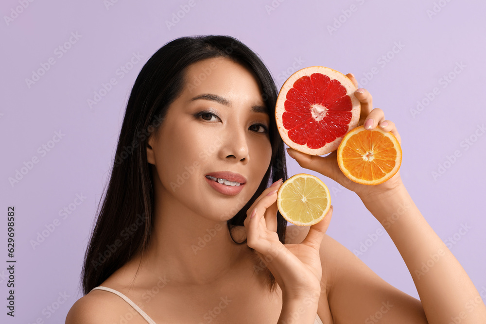 Beautiful young Asian woman with citrus fruits on lilac background