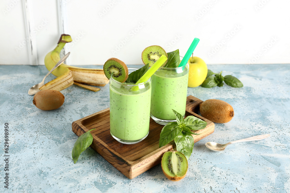 Glasses of fresh kiwi smoothie with basil on blue table