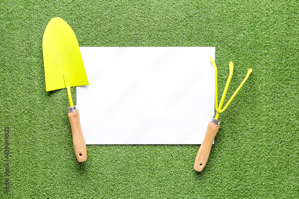 Blank paper sheet, gardening shovel and rake on color background