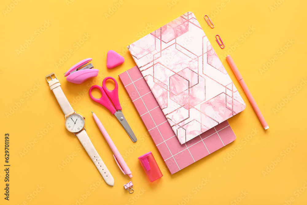 Different school stationery, notebooks and  wristwatch on orange background