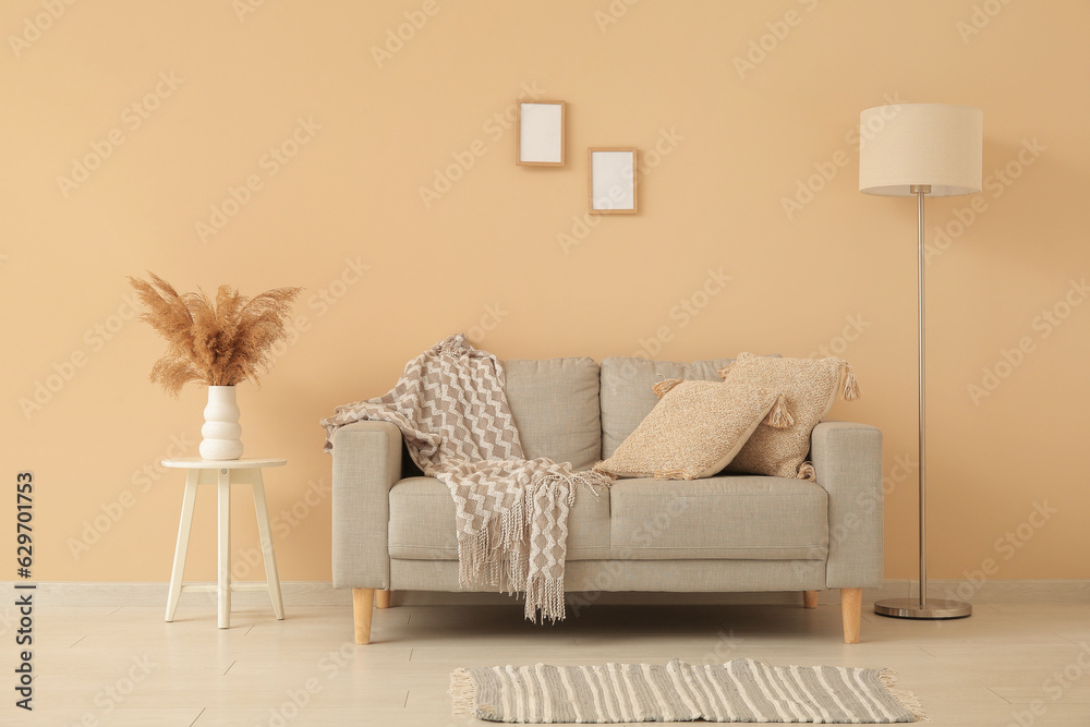 Grey sofa with cozy blanket and cushions near beige wall