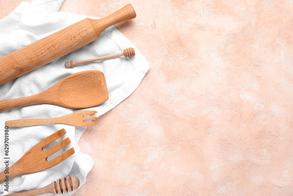 Wooden kitchen utensils and napkin on color background