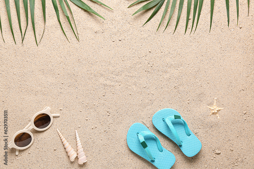 Childrens flip-flops, sunglasses and palm leaves on sand background